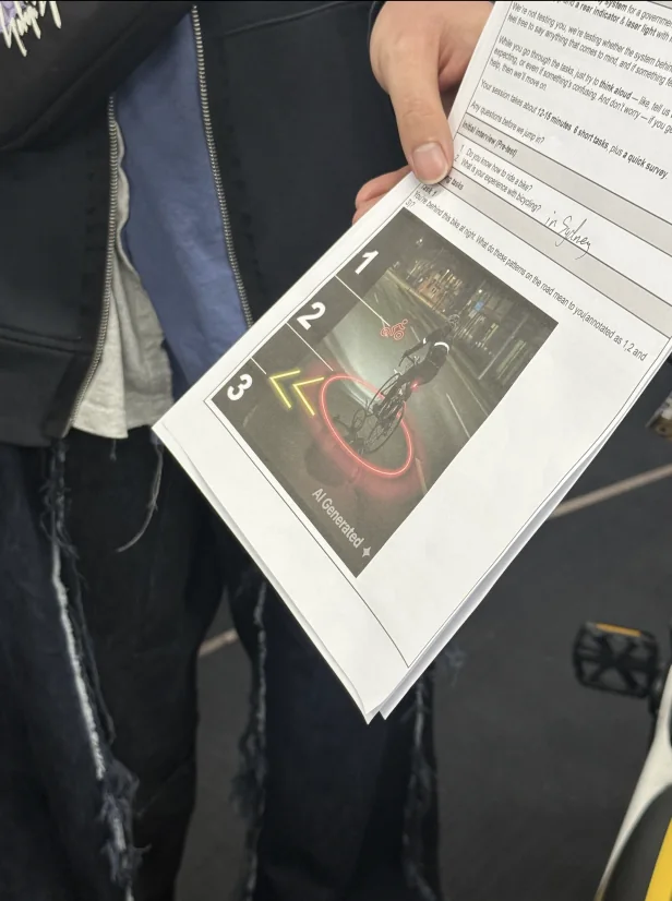 A participant holding a printed prototype sheet showing three laser patterns on the road, numbered 1 to 3