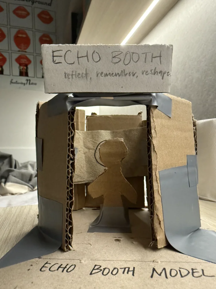 Cardboard scale model of the booth with a seated figure inside